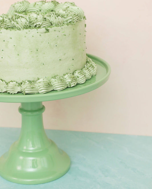 Green cake with textured frosting on a matching sage green cake stand against a light pink background