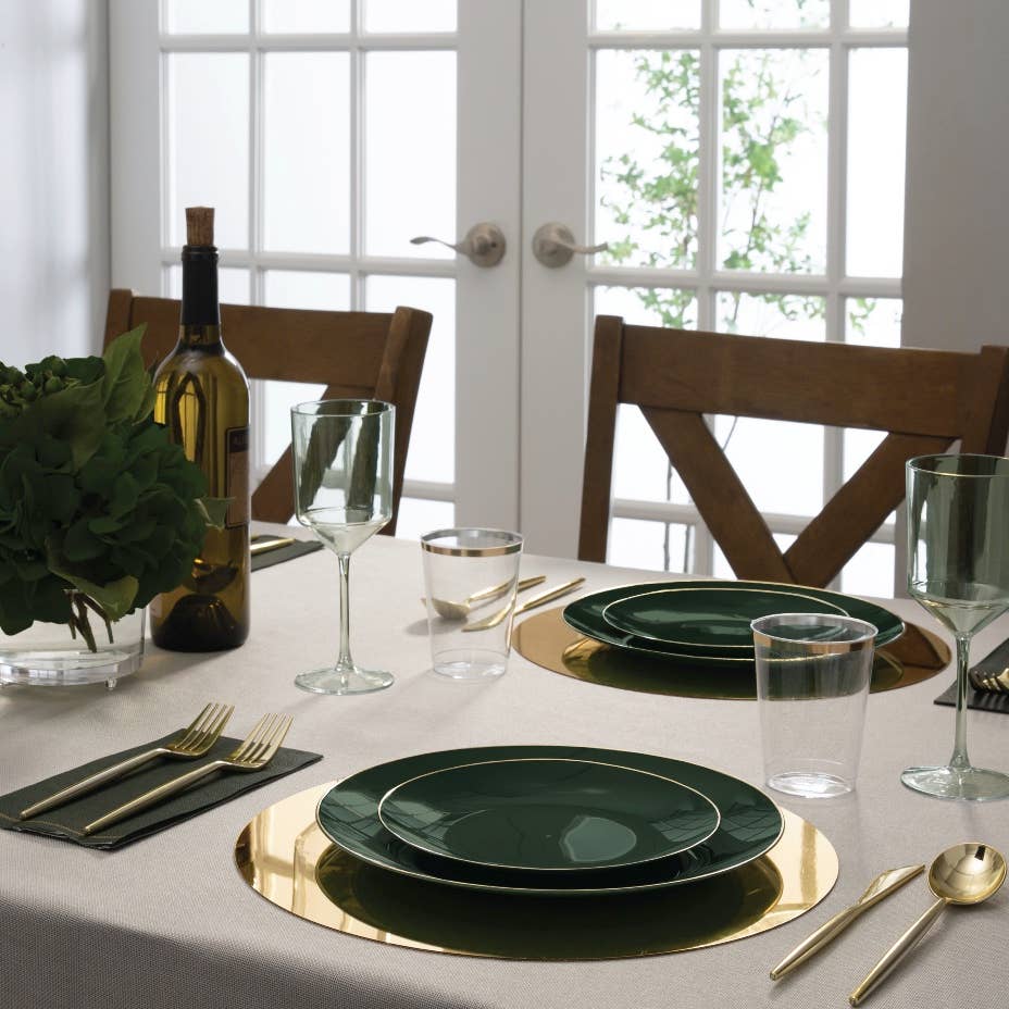 Dining table set with emerald green plates, gold cutlery, and glasses in a bright room.