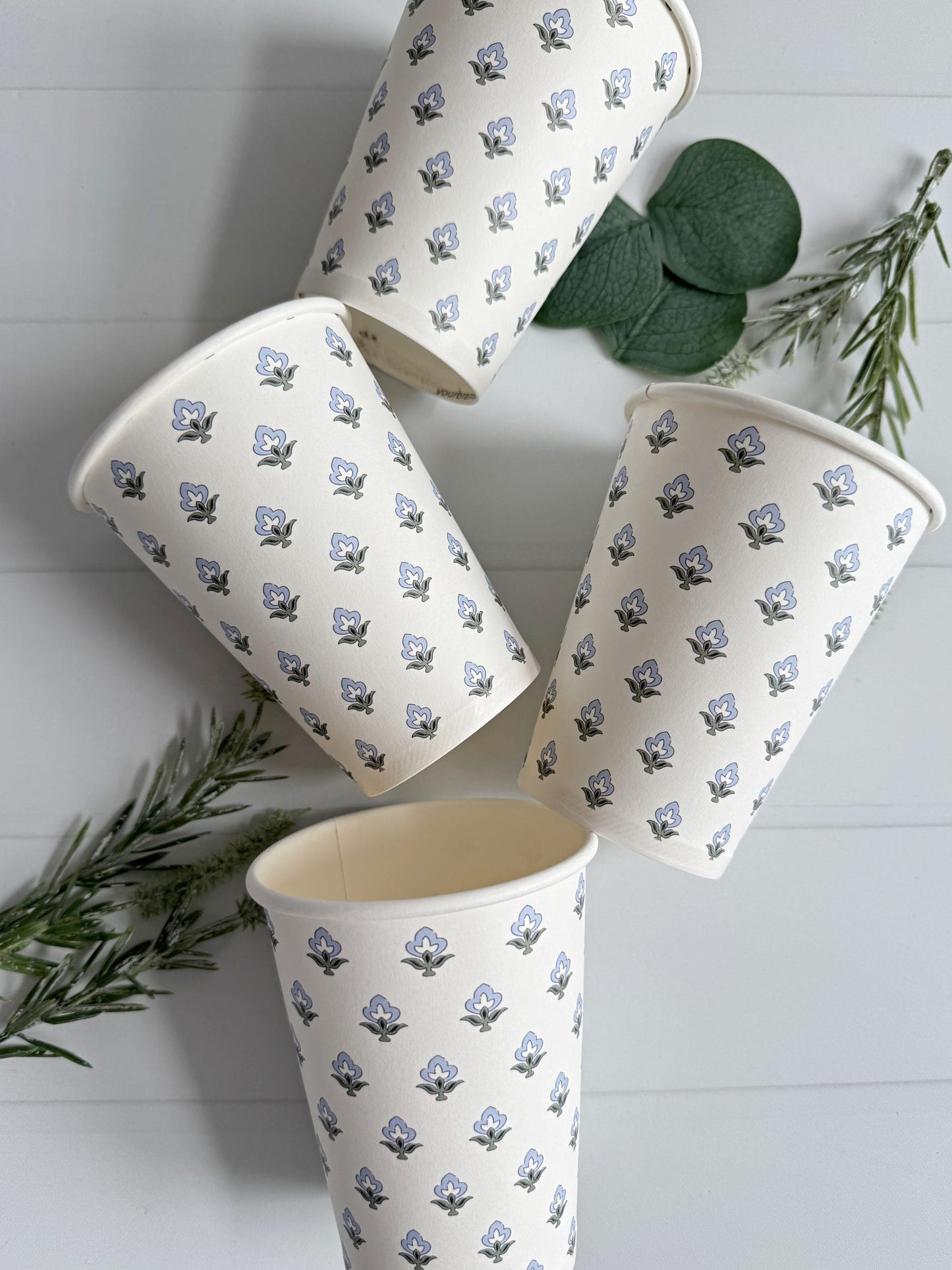 Set of four ice blue and sage block print patterned cups on a white surface with green leaves.