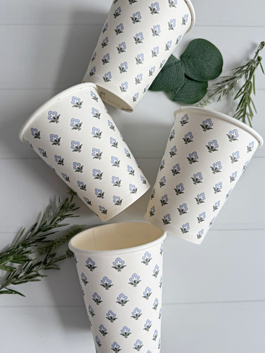Set of four ice blue and sage block print patterned cups on a white surface with green leaves.