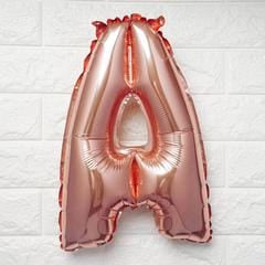 A metallic rose gold foil balloon shaped like the letter 'A', shown against a white brick wall background.