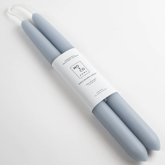 Pair of light smoke blue beeswax taper candles with a white Mo&Co label on a light gray background