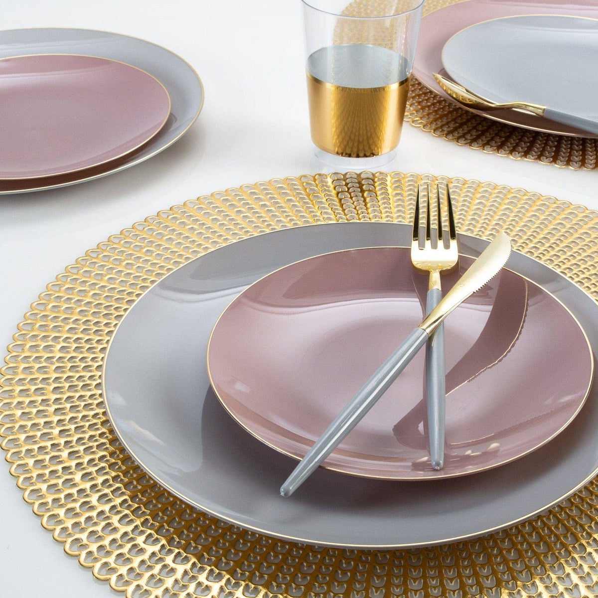 Dining table setting with pink plates, gold cutlery, and a glass of water on a white tablecloth.