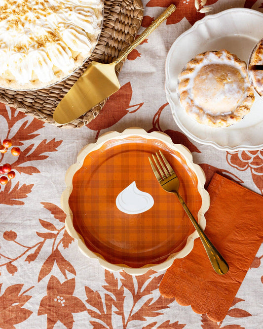 Pumpkin pie paper plate on a decorative plate with a gold fork on a patterned tablecloth.