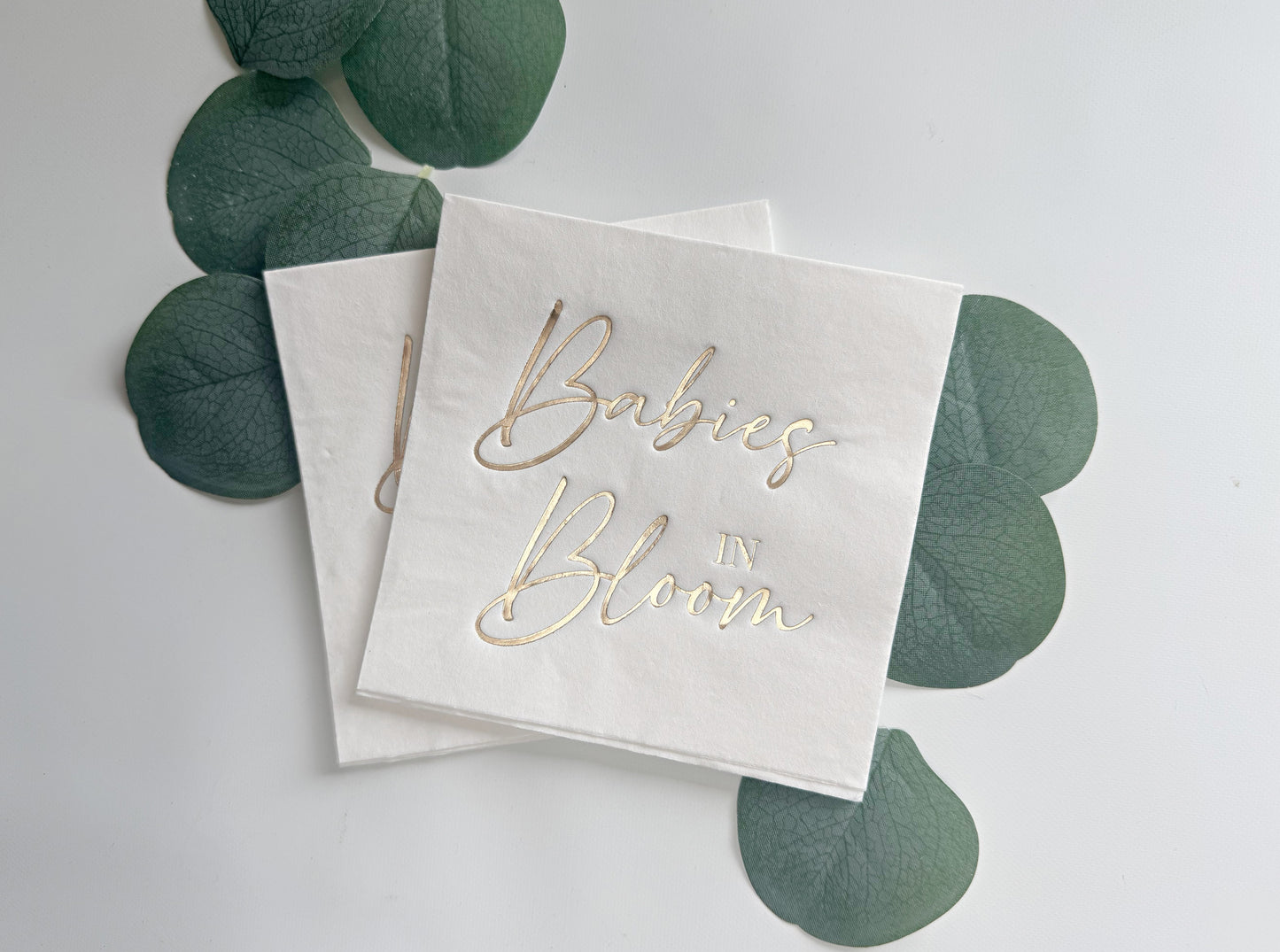 White napkins with 'Babies in Bloom' text on a light gray background with green leaves.