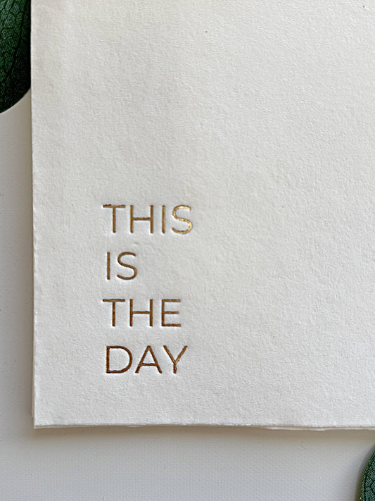 White napkins with gold text 'THIS IS THE DAY' on a light background for Christian hospitality and church coffee bar