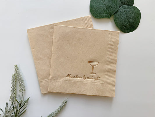 Two taupe Please Leave by Midnight paper napkins with a cocktail glass design and text on a white background with green leaves.