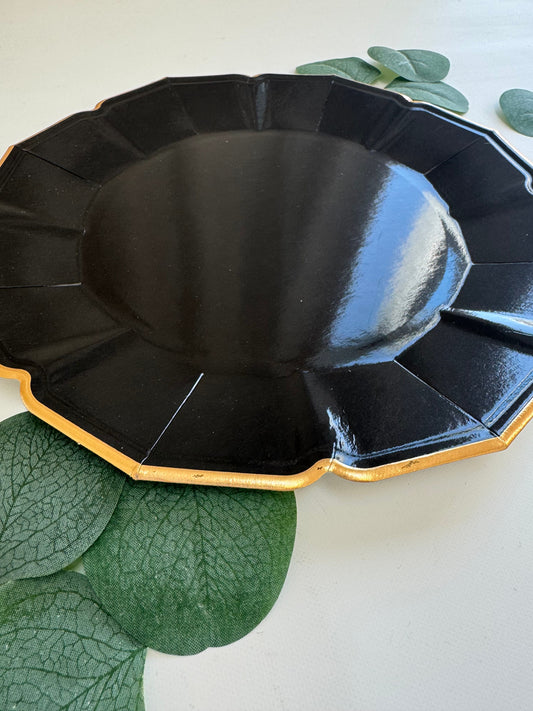 Black decorative plate with gold rim on a white background with green leaves.