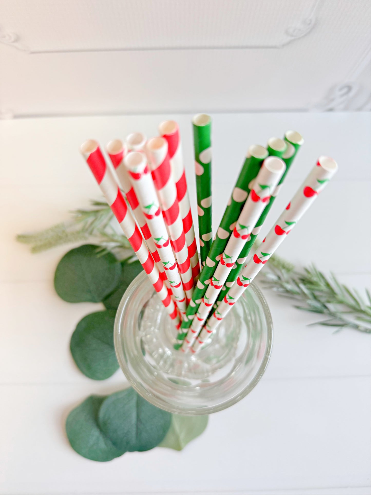 Decorative paper straws in red, white, and green with a glass jar on a light background. Features cherry prints on some straws.