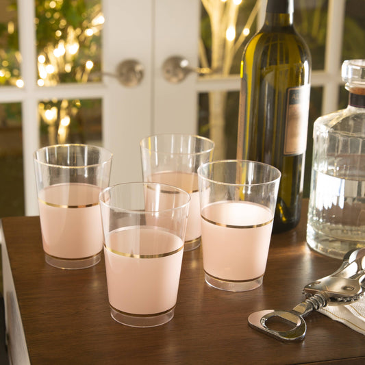 Clear glasses with pink band and gold rim on a wooden table with bottles in the background.