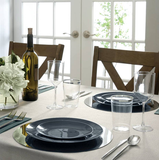 Dining table set with black plates, glasses, and silverware in a bright room.