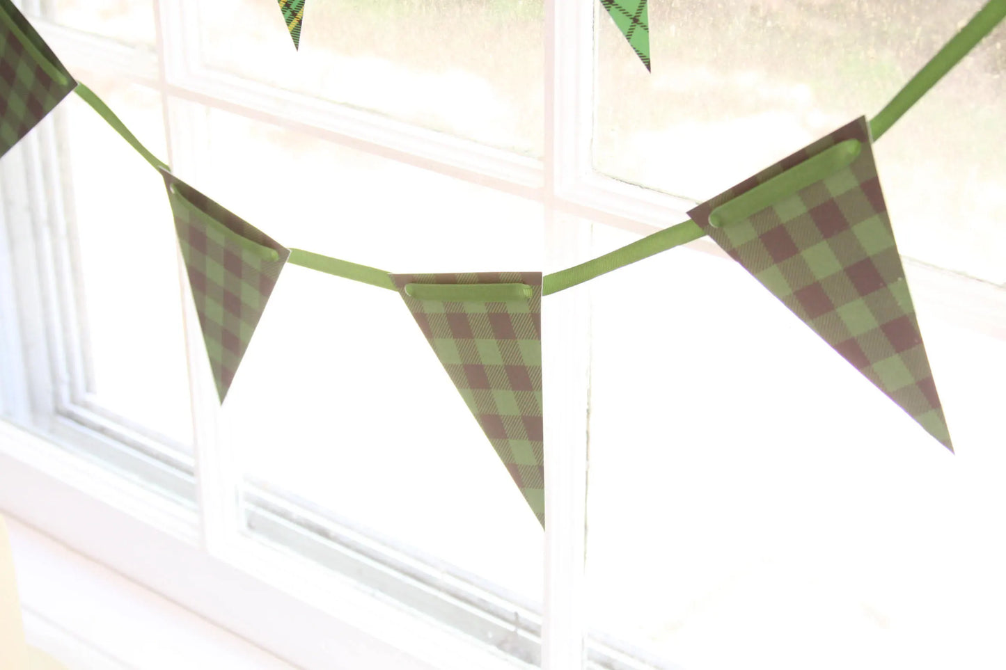 Green and black buffalo check plaid bunting banner garland hanging in front of a bright window.