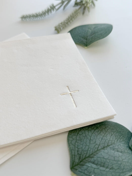 White napkins with a gold cross on a white background with green leaves.