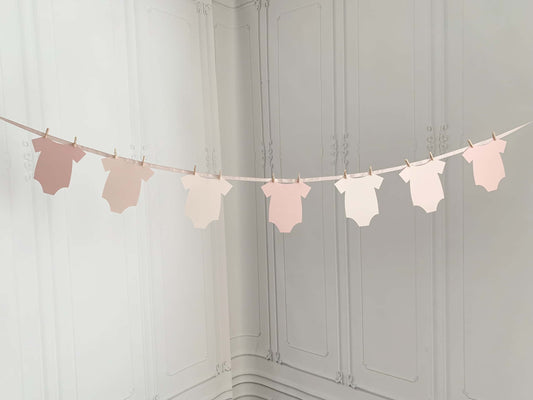Finish off your party backdrop with our shades of blush pink ombre onesie baby shower banner and delight the guests. Perfect for an Oh Baby Shower for a little girl on the way. The mom to be will love its muted colors and elegant style. Blush pink ribbon to hang like a clothesline and use the clothespins to attach the soft pink baby bodysuit cutouts. The perfect decorations for your baby shower.