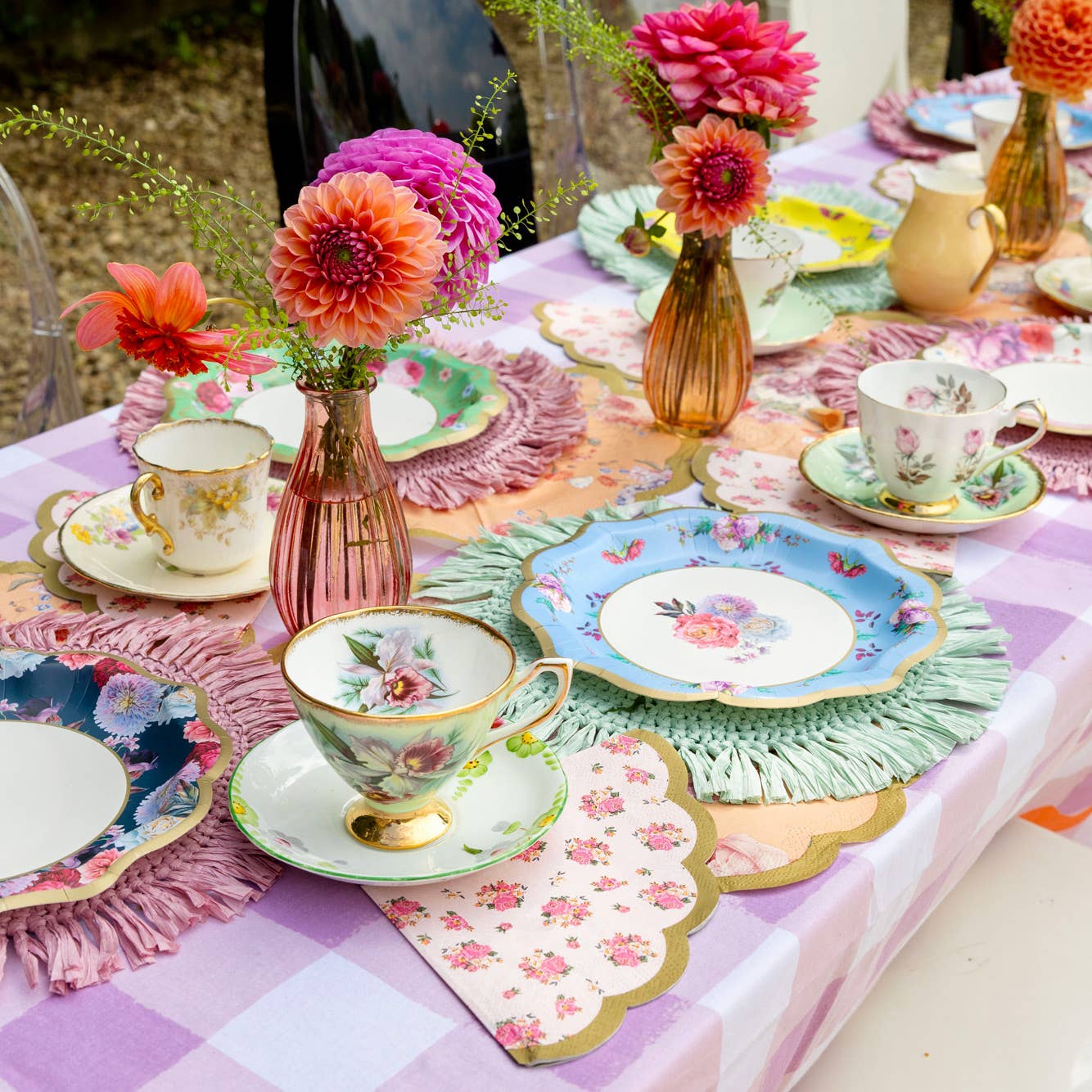 Decorative table setting with floral plates, teacups, and vases on a checkered tablecloth.