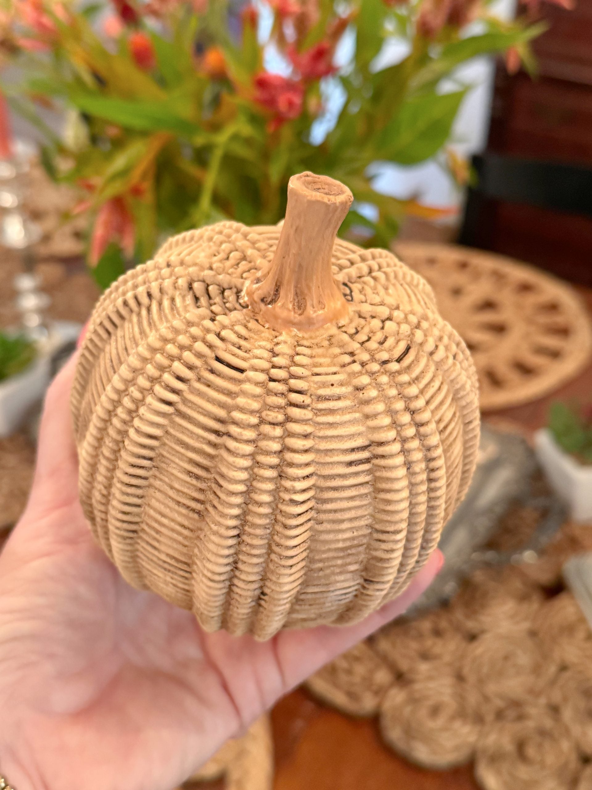 Hand holding a woven pumpkin with blurred floral background