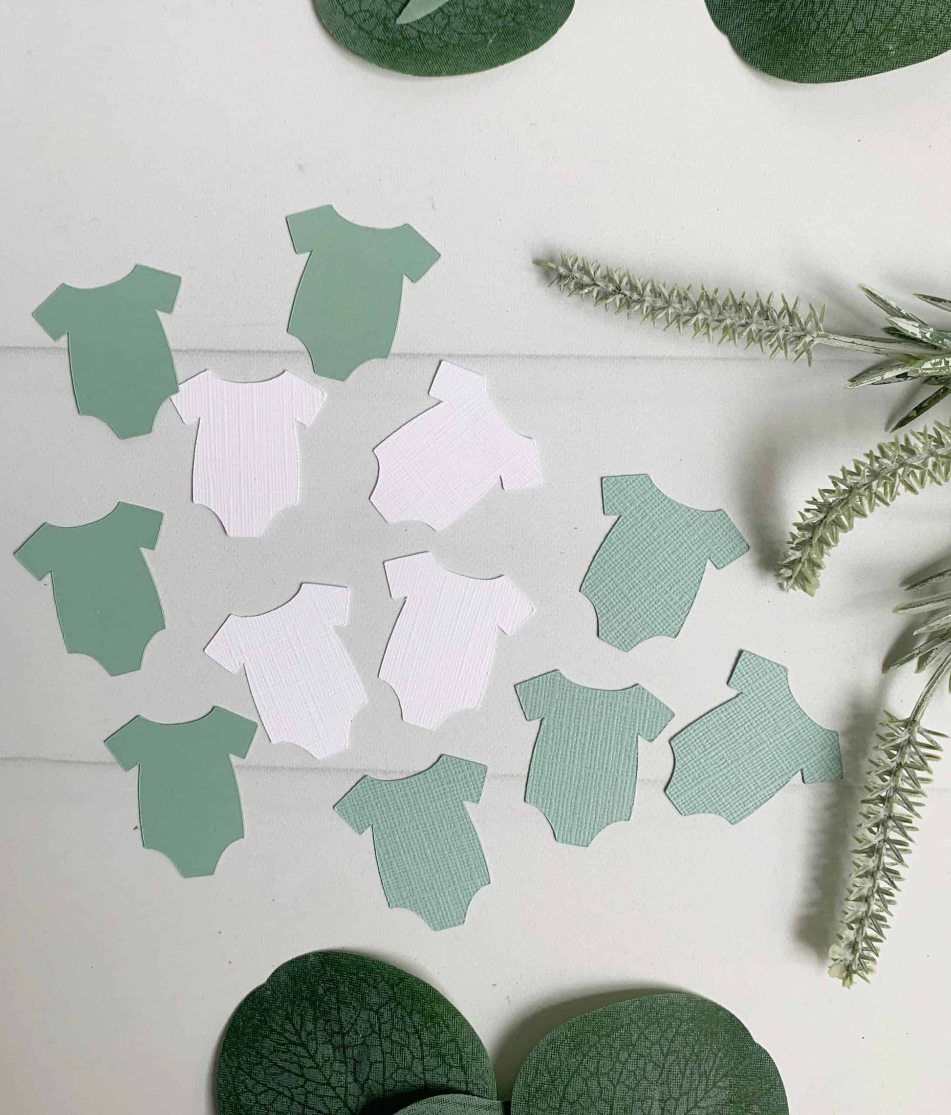 A fun addition to your baby shower party tables - these sage and white baby onesie cutouts can be spread around to decorate for a gender reveal or baby shower.