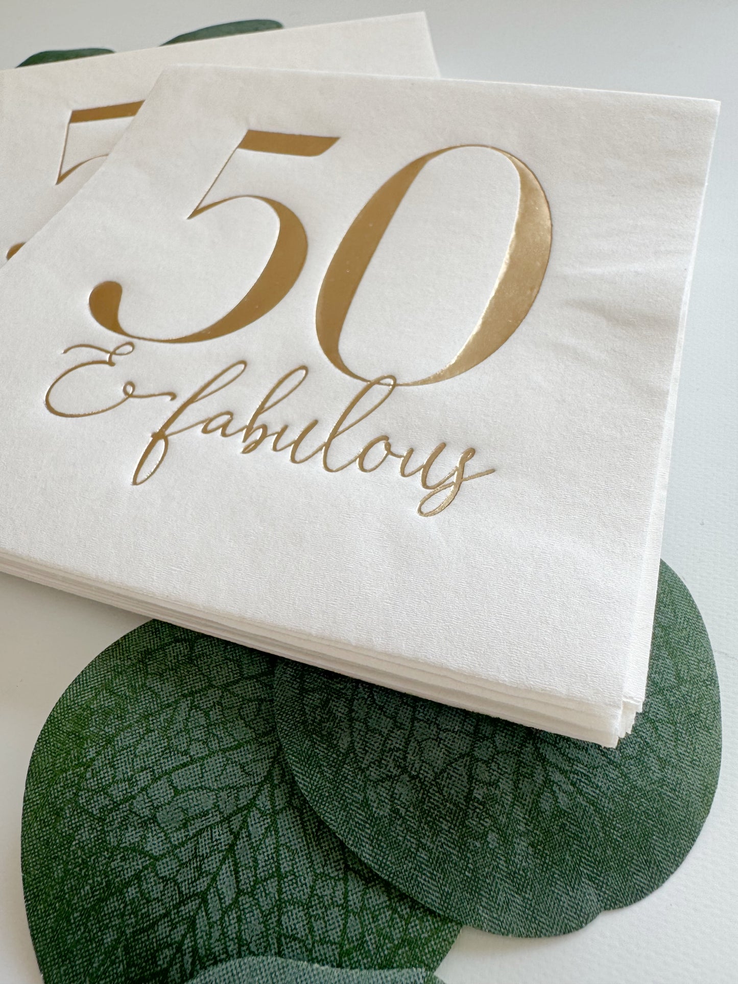 Napkin with '50 & fabulous' text on a white background showing luxurious gold foil details