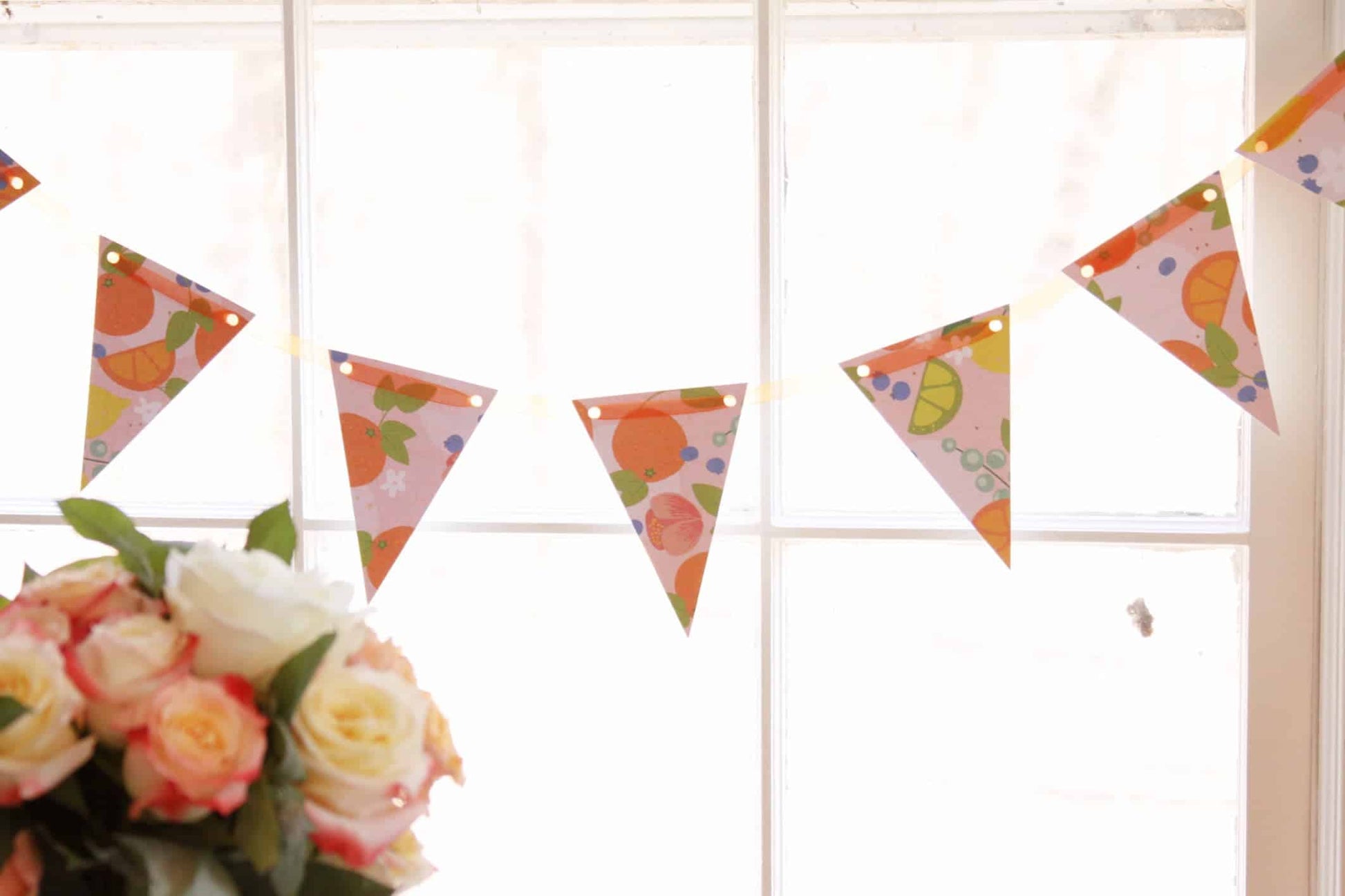 Little Cutie/Main Squeeze Pennant Banner with citrus-themed bunting flags on a pale pink background with gold foil accents, strung on a 6-foot orange sheer ribbon.
