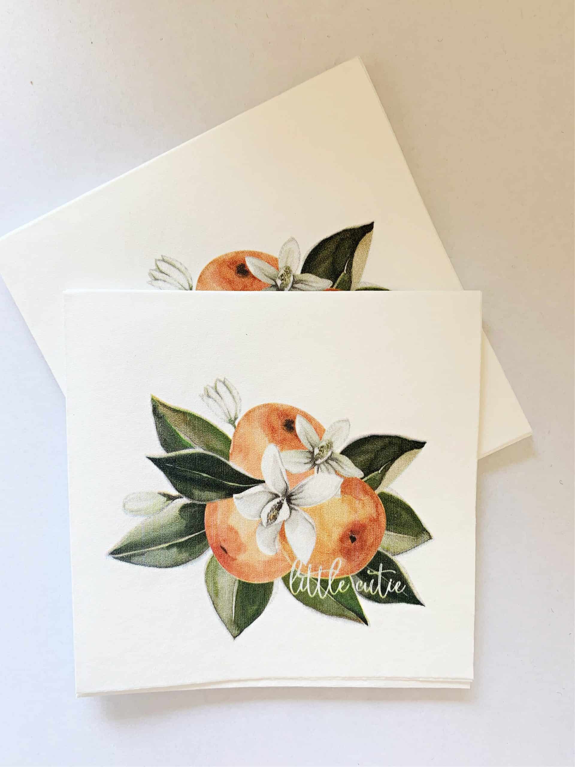 Little Cutie cocktail napkins, featuring a cluster of three clementine cuties in a modern watercolor print. Includes orange blossoms an leaves with a sweet "little cutie' white over the print for a modern touch.
