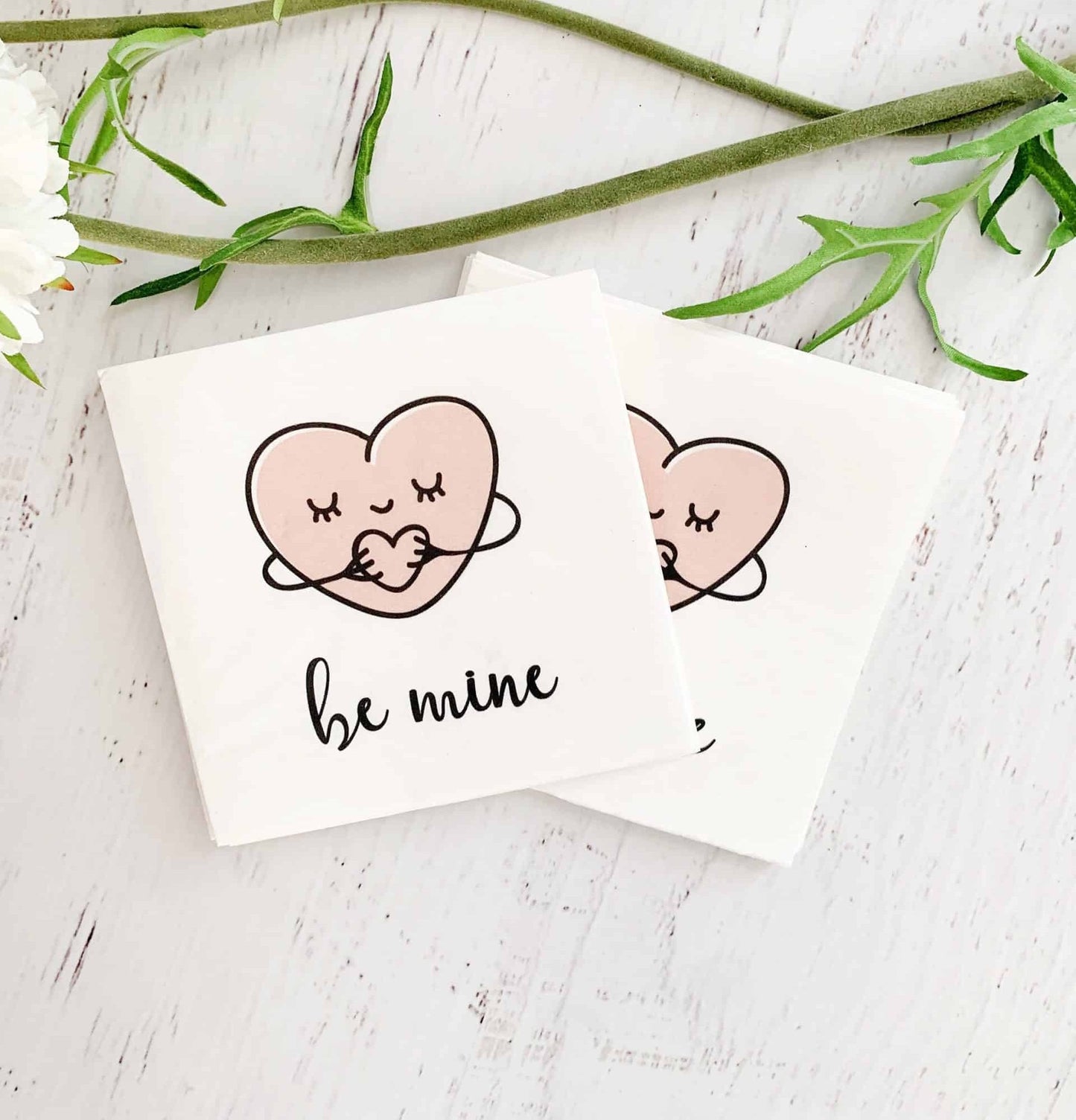 Sweet hugging hearts say "be mine" on these EnFete original cocktail napkins. White background with blush heart and black writing. Perfect for a Valentine treat, a Galentine's day cocktail, or under an afternoon snack.