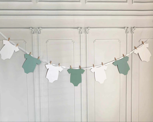 A sage baby shower onesie banner for the Little Cutie on the way! This adorable onesie-shaped banner includes white ribbon for you to hang up the onesies with the clothespins included. Perfect for a greenery or botanical baby shower.