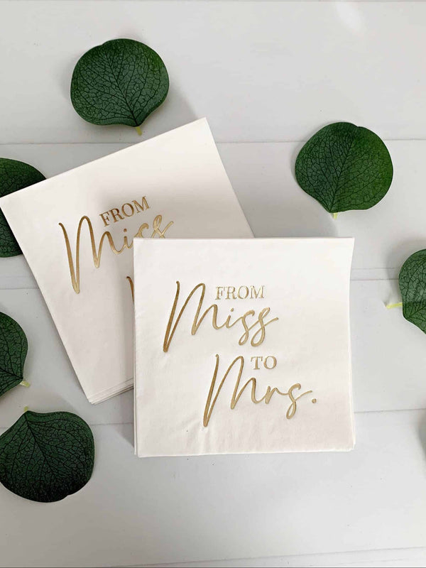 Two napkins with 'From Miss to Mrs.' text on a white surface with green leaves.