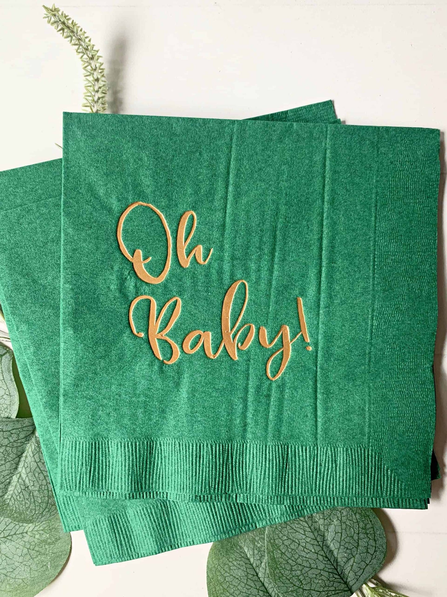 Picture of 16 'Oh Baby' luncheon napkins in gold foil script on forest green paper, perfect for a mountain adventure baby shower celebration.