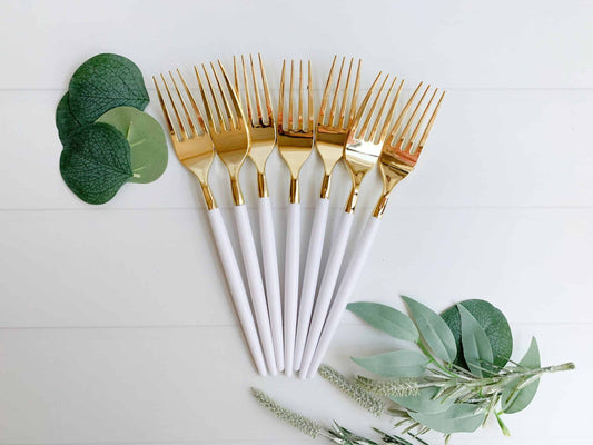 Set of gold-forked white-handled forks on a light background with green leaves.