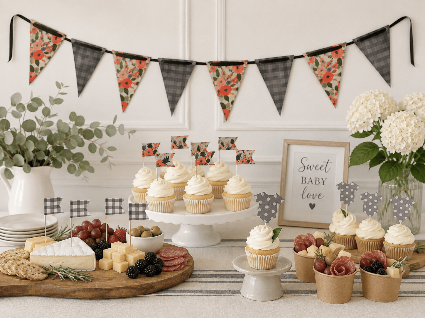 A styled baby shower dessert table with cupcakes on stands, cheese, crackers, grapes, olives, and fruit cups, decorated with floral and charcoal plaid bunting, small baby onesie picks, cupcake plaid flags, and a framed sign reading 'Sweet Baby Love'.
