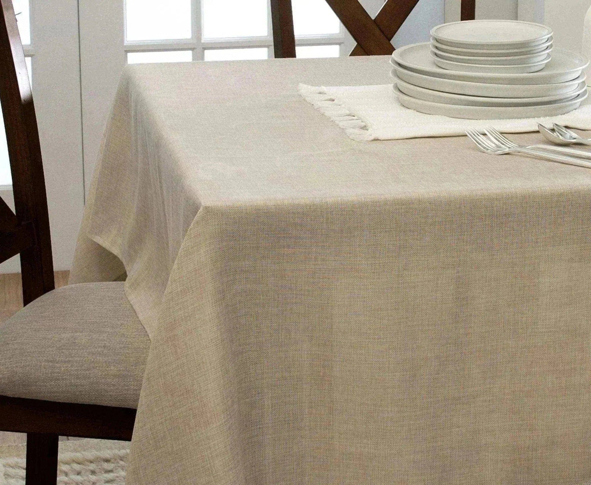 Beige tablecloth on a dining table with plates and cutlery in a bright room.