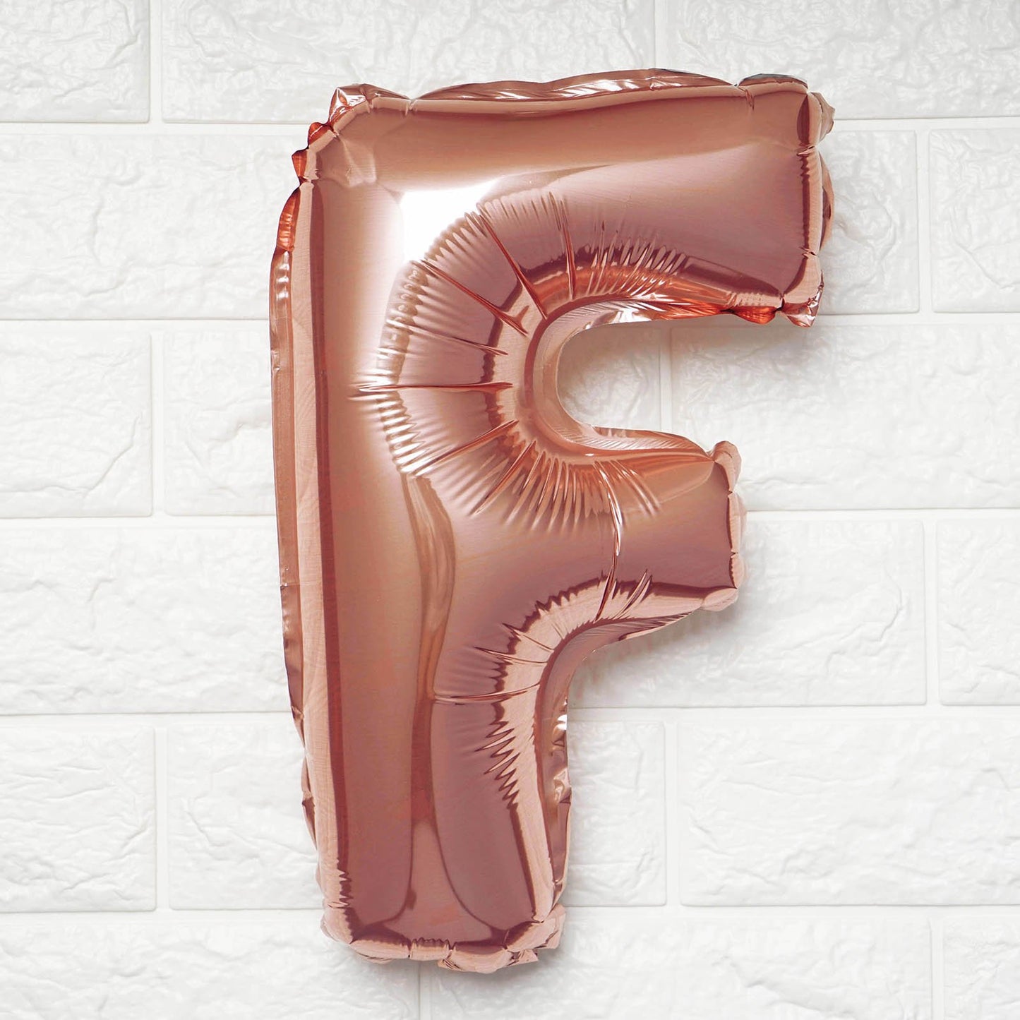 Rose gold letter 'F' balloon on a white textured background