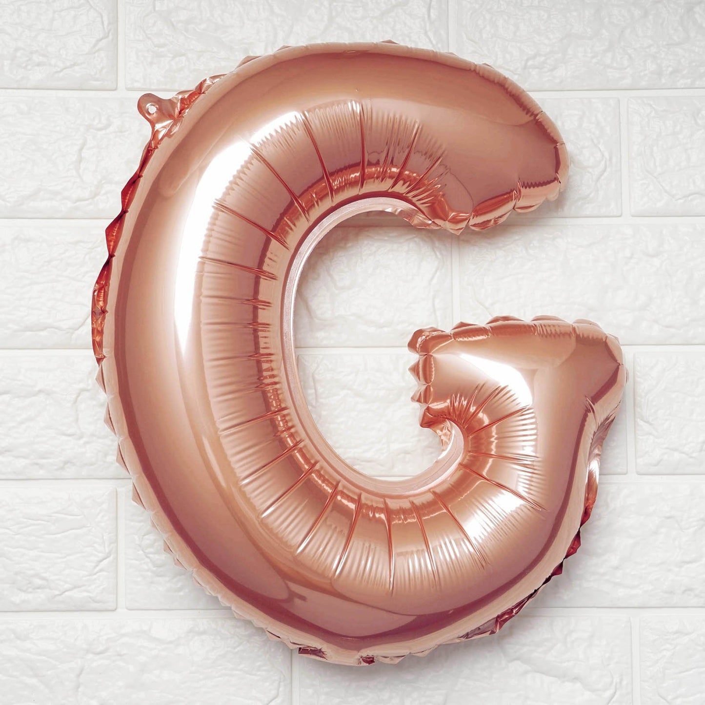 Rose gold letter 'G' balloon on a white tiled background
