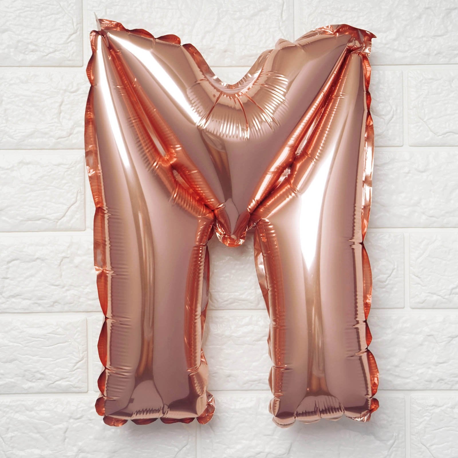 Rose gold letter 'M' balloon on a white textured background