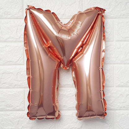 Rose gold letter 'M' balloon on a white textured background