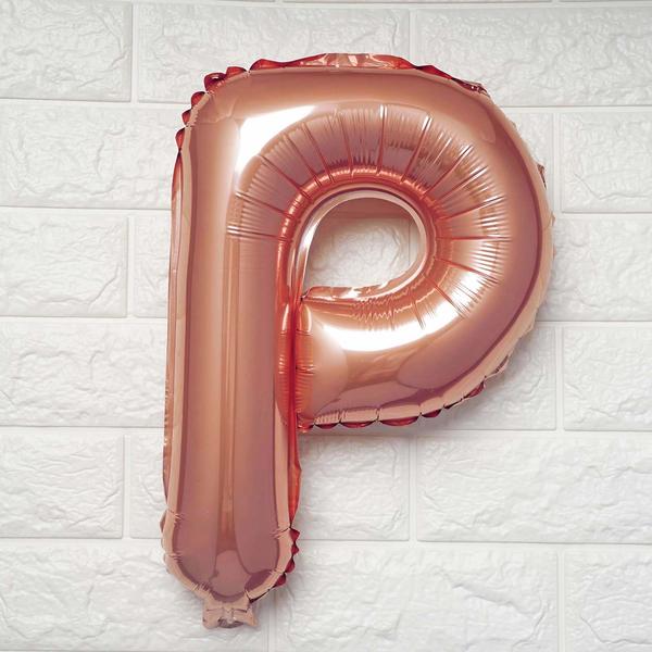 A metallic rose gold foil balloon shaped like the letter 'P', shown against a white textured brick wall background.