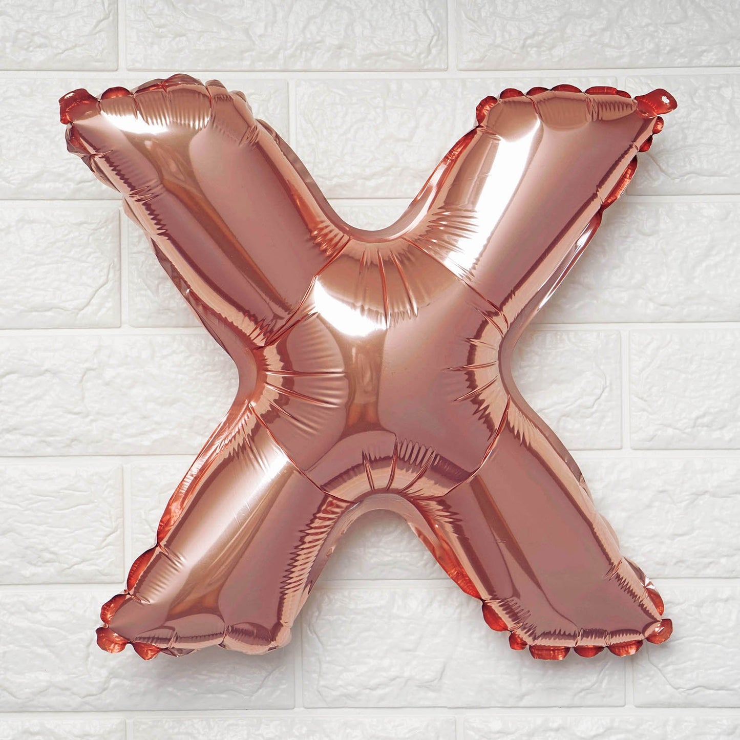 Rose gold letter 'X' balloon on a white textured background