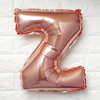 A metallic rose gold foil balloon shaped like the letter 'Z', floating against a white textured brick wall background.