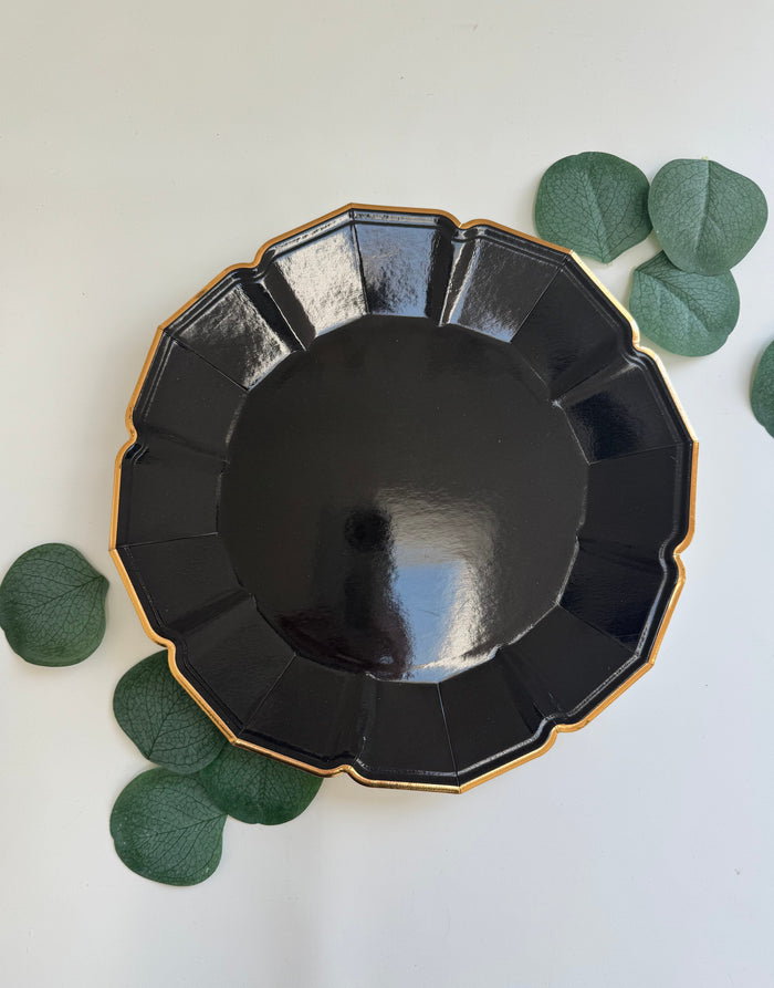 Black decorative plate with gold rim on a white background with green leaves.
