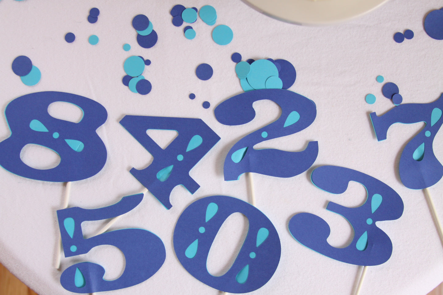 Blue and light blue paper number cutouts on a white surface, party decorations or cake toppers.