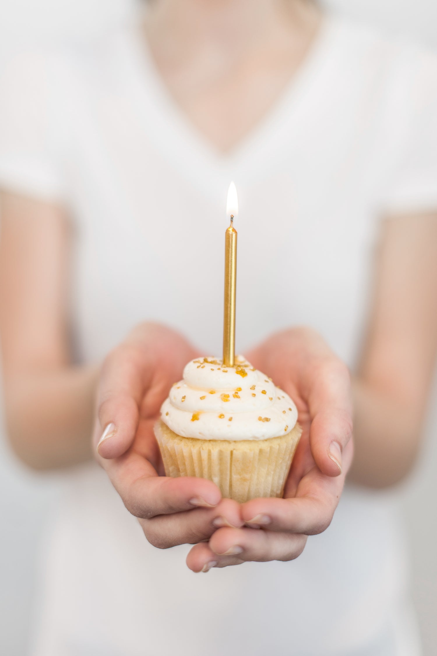 Person holding a cupcake with a lit golden candle against a white background - elegant party supplies for home celebrations