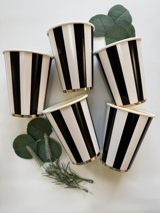 Set of black and white striped party cups on a white surface with green leaves.