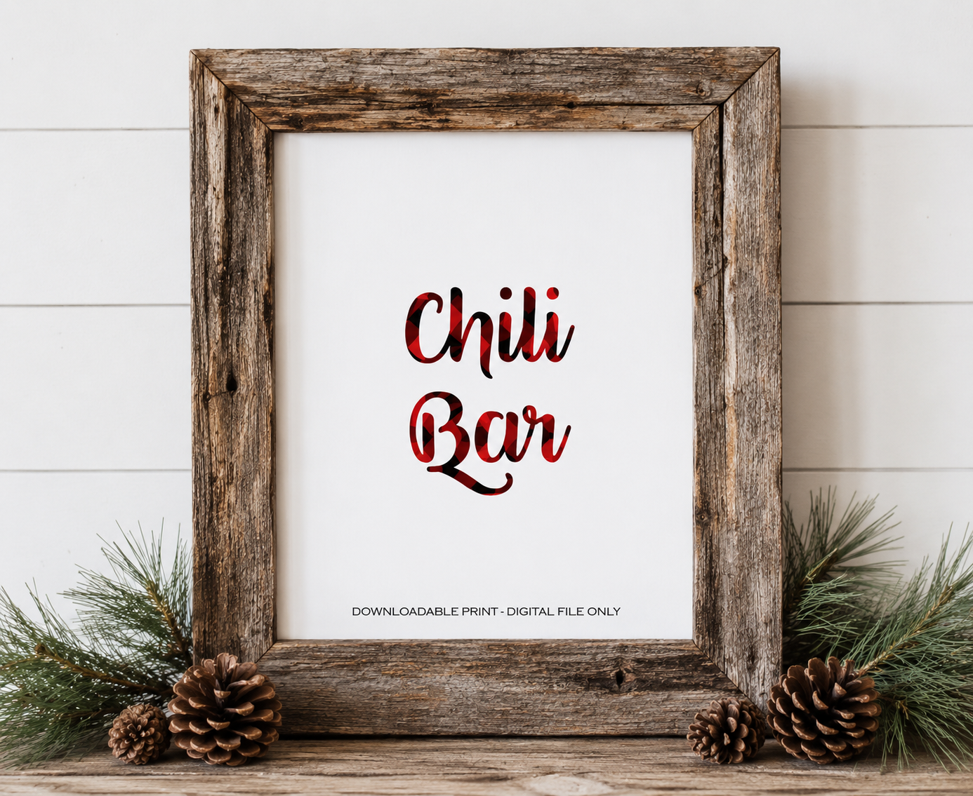 A rustic wooden framed print with the words 'Chili Bar' in red and black plaid-style lettering on a white background. The frame is styled on a wooden surface with pine branches, pinecones, and a white shiplap wall behind it.