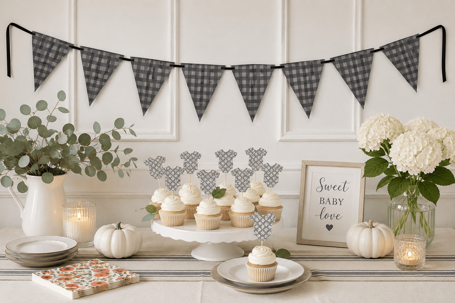 A styled fall-themed party table setup featuring a black and white gingham bunting banner, cupcakes on a white cake stand, white pumpkins, a vase of green eucalyptus, white hydrangeas, and a framed sign that reads 'Sweet Baby Love'.