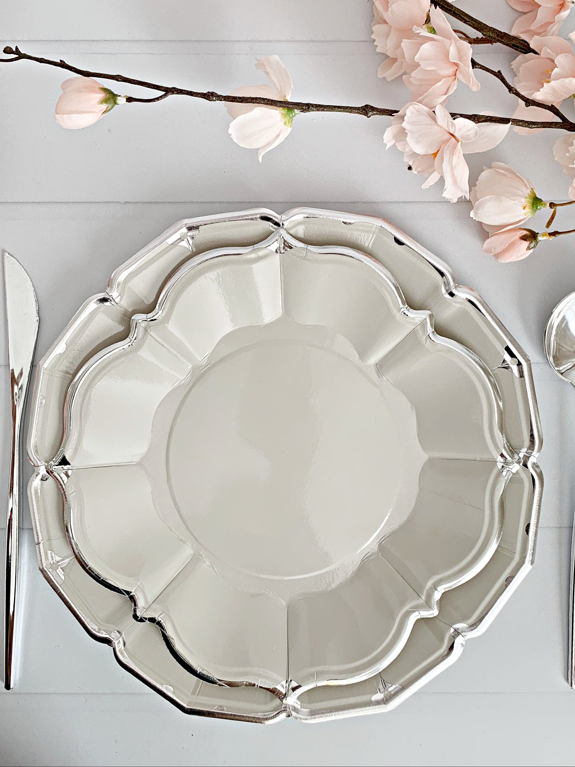 Elegant table setting with a decorative plate, silverware, and pink flowers on a light gray surface.