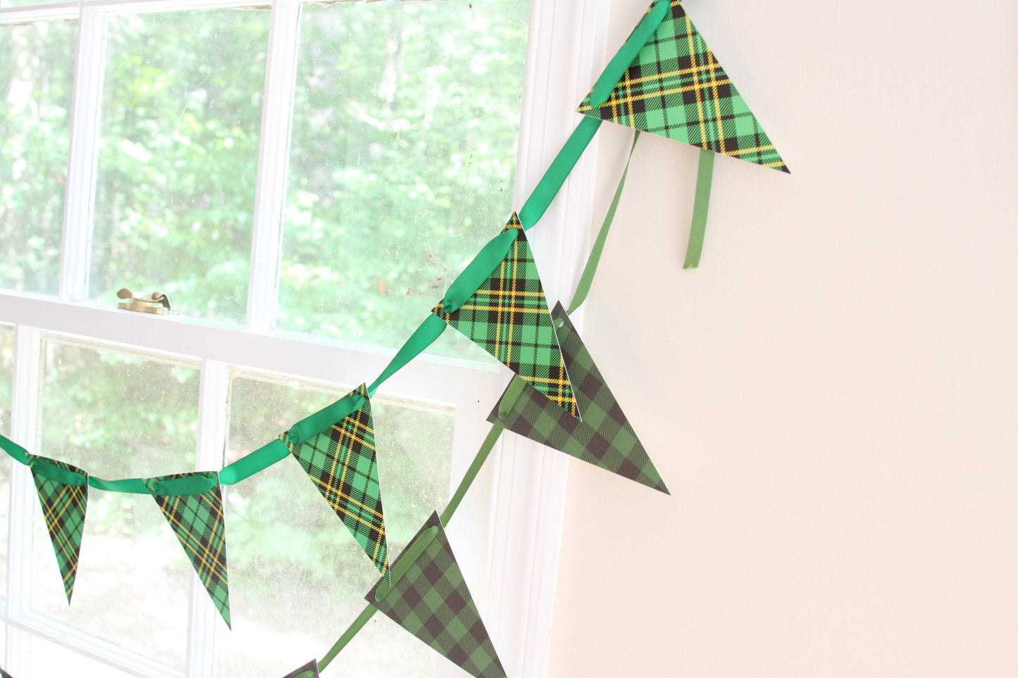 Green tartan plaid triangular bunting banner garland hanging on a wall next to a window.