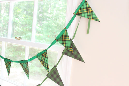 Green tartan plaid triangular bunting banner garland hanging on a wall next to a window.
