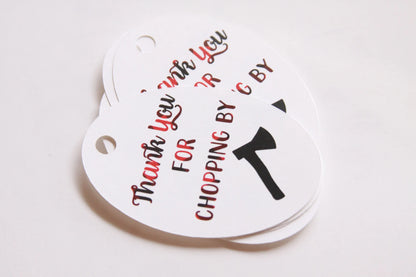 A stack of white oval gift tags with hanging holes, printed with the phrase 'Thank you FOR CHOPPING  BY' in red and black lettering alongside a black axe graphic, on a plain white background.