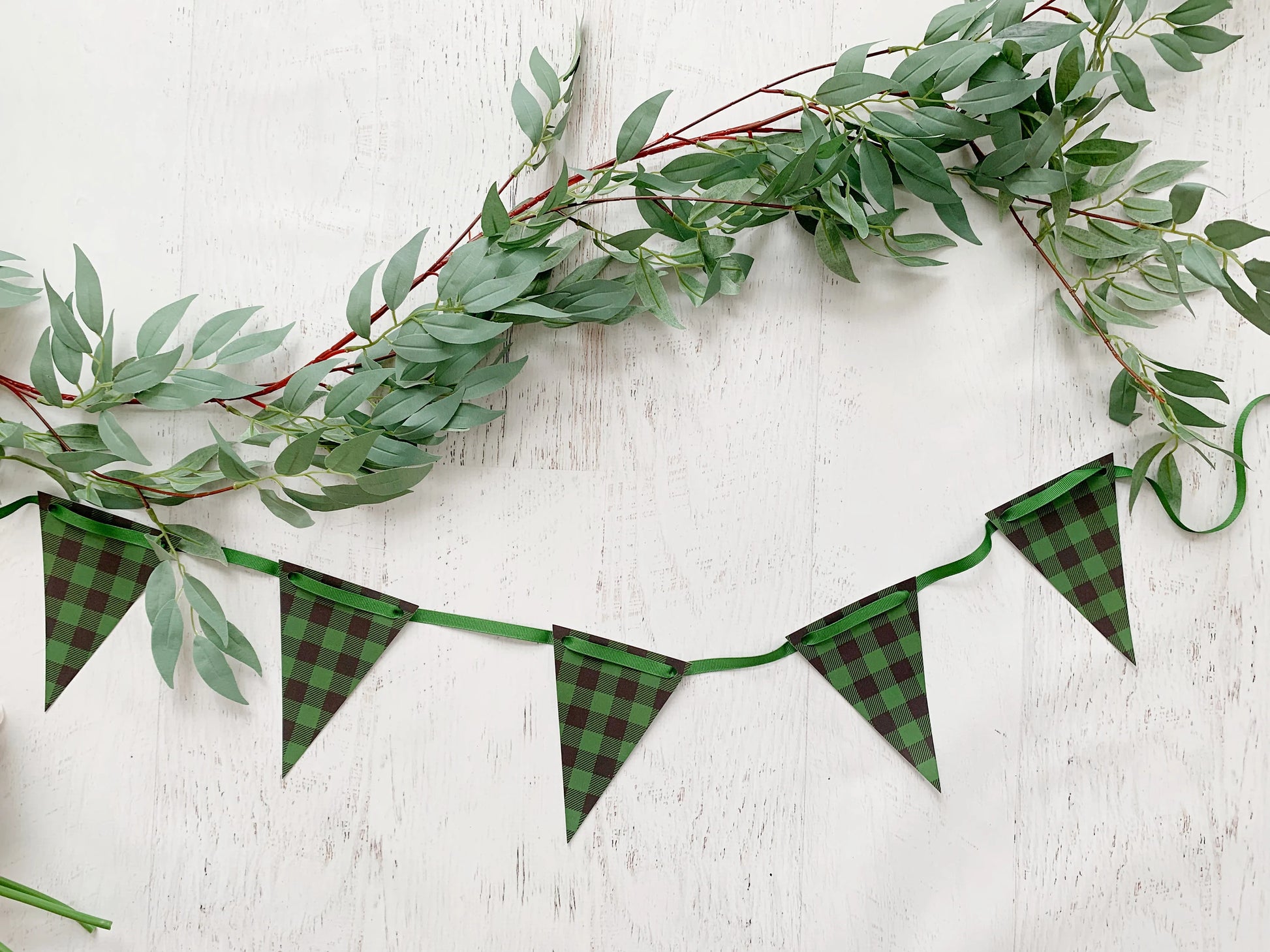 Green buffalo plaid bunting banner garland with triangular flags and a green ribbon, styled with a green eucalyptus garland on a white wood background.