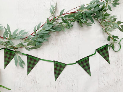 Green buffalo plaid bunting banner garland with triangular flags and a green ribbon, styled with a green eucalyptus garland on a white wood background.